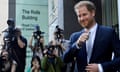 A smiling Prince Harry outside the Royal Courts of Justice, with numerous photographers in the background.