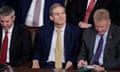 Middle-aged white man in yellow tie and suit looking grim between two white men looking down