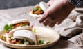 Man's hands hold asian sandwich steamed gua bao buns with pork belly, greens and vegetables served in ceramic plate on table with linen tablecloth. As<br>P8GK5N Man's hands hold asian sandwich steamed gua bao buns with pork belly, greens and vegetables served in ceramic plate on table with linen tablecloth. As