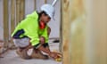 A female worker wearing hi-vis clothing, a hardhat and boots works on a construction site