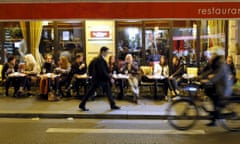 A man walks on the street as people sit at a table outside a bistro in Paris, France.
