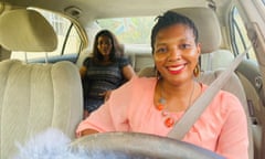 A smiling woman driving a car with a passenger on the back seat in Lagos, Nigeria