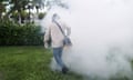 person wearing white top, jeans and black shoes holds yellow and black machine above grass as smoke billows