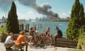 USA. Brooklyn, New York. September 11, 2001. Young people relax during their lunch break along the East River while a huge plume of smoke rises from Lower Manhattan after the attack on the World Trade Center.