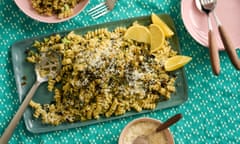 A green rectangular plate with fusilli topped with rough broccoli sauce, breadcrumbs, lemon wedges and cheese. It sits on a green tablecloth.