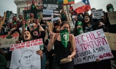 A group of largely female protesters, many in balaclavas wave placards and flags as a woman in the front