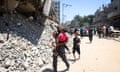 A man carries children next to rubble from destroyed buildings.