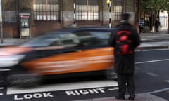 a person waits to cross a zebra crossing in London while a car passes