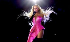 Beyoncé performs onstage wearing a bright pink dress as her hair is blown into the air