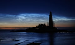 Lighthouse at dusk with illuminated clouds in sky above sea