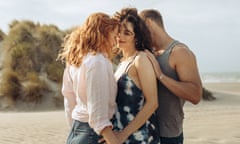 Eleanor Tomlinson, Jessica De Gouw and Sam Heughan huddled close together on a beach.