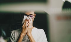 A boy wearing glasses holding a tissue to his nose