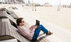 Man using laptop sitting on a wooden sunbed on the beach<br>GettyImages-666023330