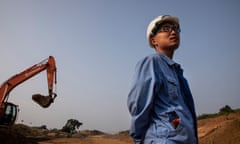 A man in a hard hat stands before a digger in Sri Lanka