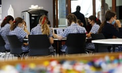 Students sit around a table in a school classroom, some are wearing face masks