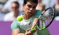 Close-up of Carlos Alcaraz, in the sun, wearing a striped shirt and hitting a tennis ball with his racquet