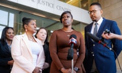 Woman wearing brown dress flanked by man and woman in front of microphone at press conference