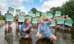 Two people crouching in river talking animatedly, with group of people in river behind holding up Green Party signs.