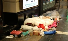 Homeless person in sleeping bag on street, surrounded by belongings