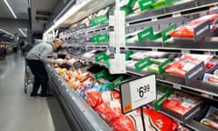 A customer stoops down to look at meat products at a grocery store. A nearby price sign advertises chicken leg quarters for $6.99 per package.