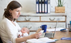 A woman holding her baby and a phone in front of a laptop