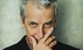 Peter Capaldi, head and shoulder shot, holding his hand to his mouth and looking up; wearing a black jacket and brown shirt