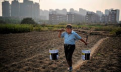 A man carries buckets of water across a vegetable field near a new residential compound in Hefei, Anhui province, China