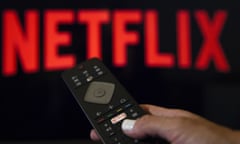 A person holds a remote control in front of the Netflix logo