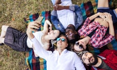 friends in casual summer wear lying in circle on the colourful rug in the park having fun and making a group selfie