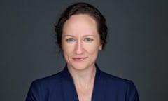 A studio portrait of a young white woman with blue eyes, brown hair loosely pulled back, a friendly, right-on look at the camera, and a blue blazer with a white top.