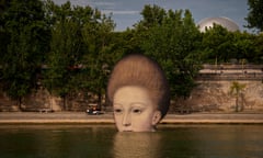 A colossal painted head of a woman partially submerged in the water by the bank