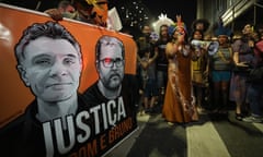 Indigenous people hold a banner showing images of Dom Phillips and Bruno Pereira at a nighttime protest