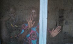 Two young African women look through an insect screen over a window