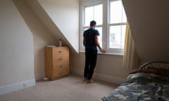 A young male, who is an unaccompanied asylum seeker, stands his bedroom