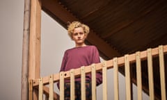 julia garner hands in pockets on a wooden railed balcony