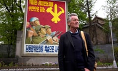 Michael Palin in North Korea<br>Michael Palin in North Korea - Channel 5 Press publicity still Michael Palin standing next to a propaganda poster