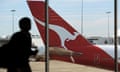 A passenger walking inside a terminal past the tail of a Qantas plane at the Sydney International Airport.