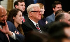 A man wearing glasses, suit, and tie stands in a crowd