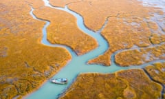 A small fishing boat navigating a complex pattern of rivulets in a grassy and partially submerged estuary