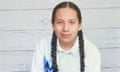 A teenage boy wearing a white button-down with a blue design and two braids smiles