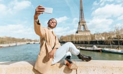 Woman sitting on bridge over the river Seine with the Eiffel tower in the background taking a selfie