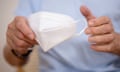 Stock image of man in blue Oxford shirt holding white face mask.