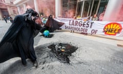 Acitivists in black stand next to oil slicks on the pavement, and others hold a banner that reads 'largest shareholder of Shell'