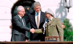 Yitzhak Rabin and Yasser Arafat shake hands as Bill Clinton gestures expansively