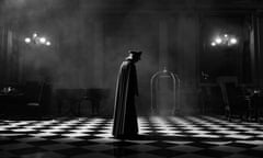 a black and white still of a man looking down at a black and white tiled floor in a grand room, wearing a soldier's hat and a cloak