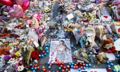 Dozens of packaged flowers cover a paved surface, with colourful candles and balloons interspersed around a photo of Ariana Grande