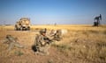 Troops kneel near oil equipment and military vehicle