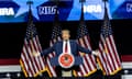 man in a suit with arms outstretched in front of american flags