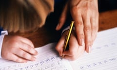 Left-handed child practising writing in book, guided by adult.