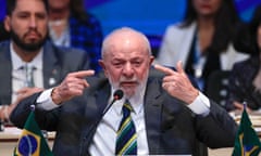 A white man in a suit bnext to Brazil's flag gestures while speaking at a conference